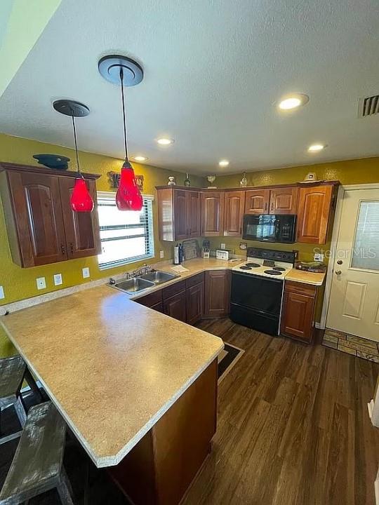 kitchen with kitchen peninsula, white electric range oven, pendant lighting, dark wood-type flooring, and sink