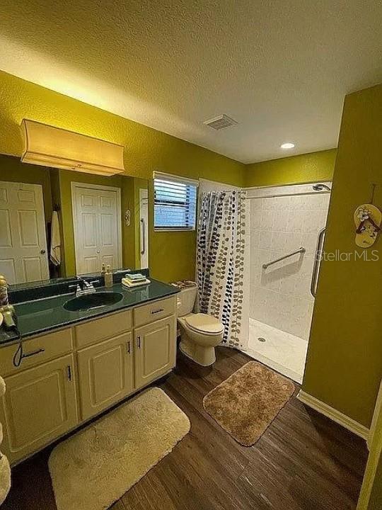 bathroom featuring a textured ceiling, curtained shower, wood-type flooring, vanity, and toilet