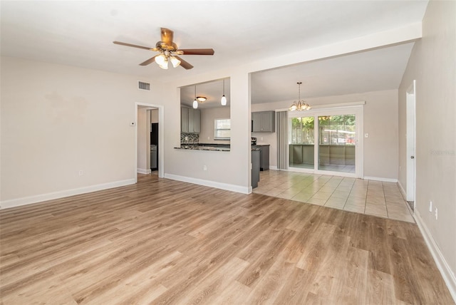 unfurnished living room featuring ceiling fan with notable chandelier and light hardwood / wood-style flooring