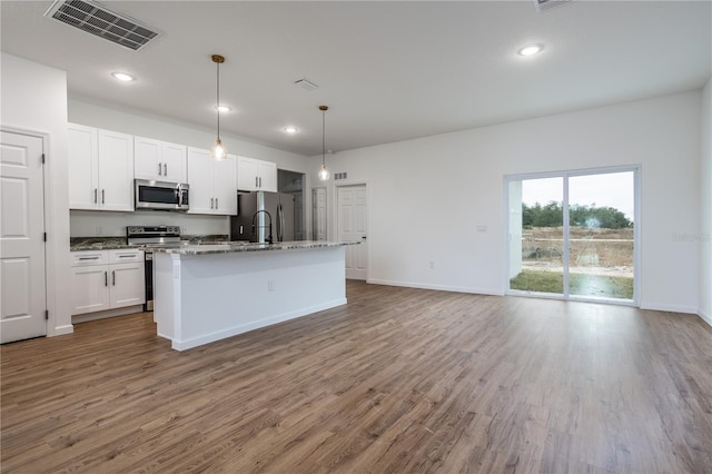 kitchen with light stone countertops, white cabinetry, hardwood / wood-style floors, a kitchen island with sink, and appliances with stainless steel finishes