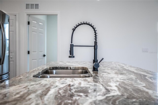 kitchen with stainless steel fridge, sink, and light stone counters