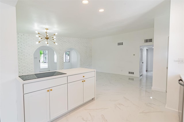 kitchen featuring brick wall, light tile floors, black electric cooktop, an inviting chandelier, and white cabinetry