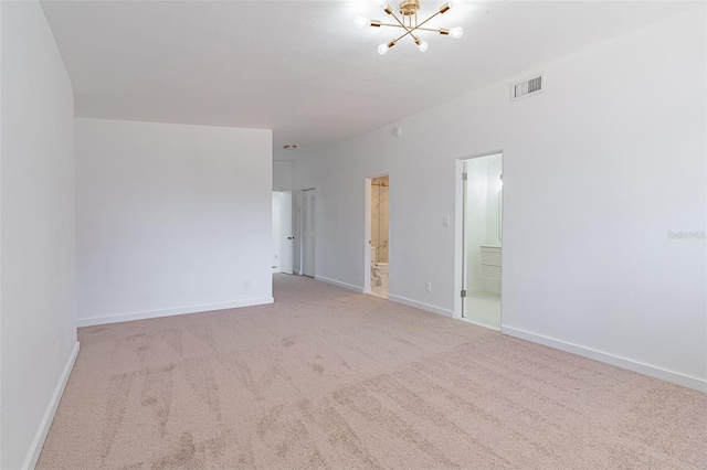 spare room with a notable chandelier and light colored carpet