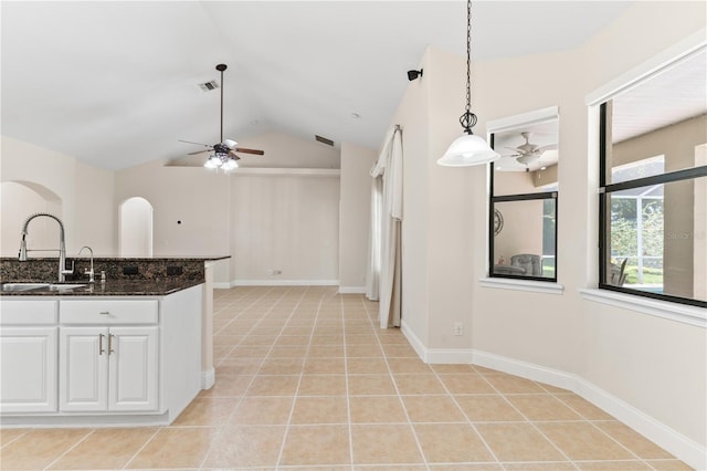 kitchen with lofted ceiling, sink, hanging light fixtures, dark stone countertops, and white cabinets