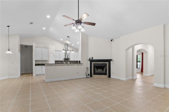 unfurnished living room with a tiled fireplace, light tile patterned floors, high vaulted ceiling, and ceiling fan