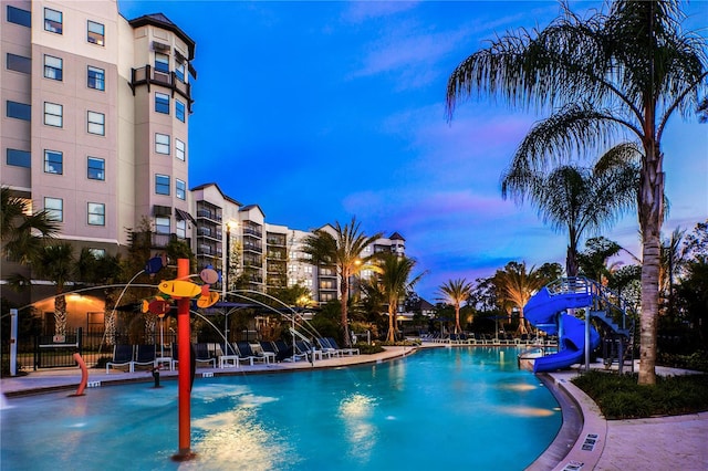 pool at dusk with pool water feature and a water slide