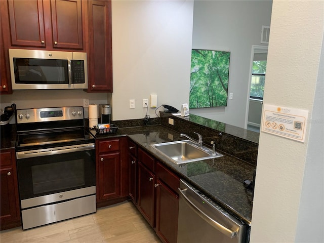 kitchen with dark stone counters, sink, light wood-type flooring, kitchen peninsula, and stainless steel appliances