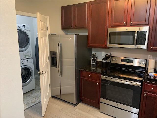 kitchen featuring light hardwood / wood-style floors, dark stone countertops, stacked washing maching and dryer, and appliances with stainless steel finishes