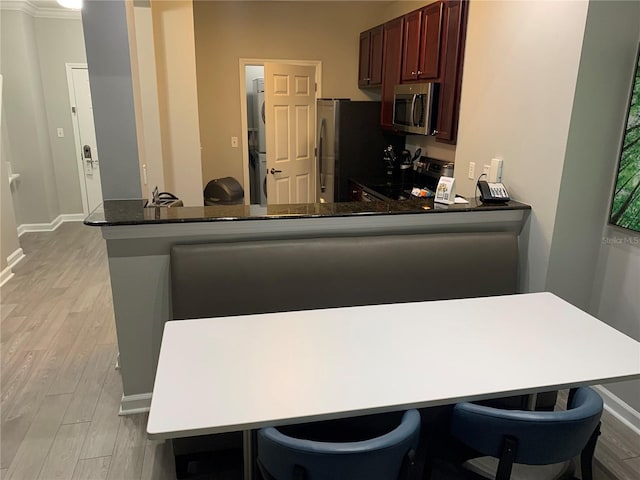 kitchen with stainless steel appliances, kitchen peninsula, dark stone counters, a breakfast bar, and light wood-type flooring