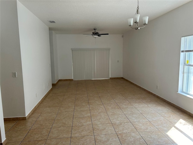 empty room with a textured ceiling, ceiling fan with notable chandelier, and light tile patterned floors