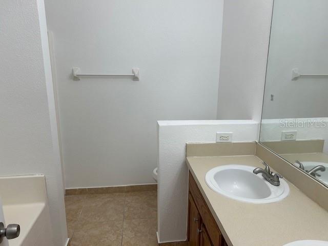 bathroom featuring toilet, vanity, a washtub, and tile patterned floors