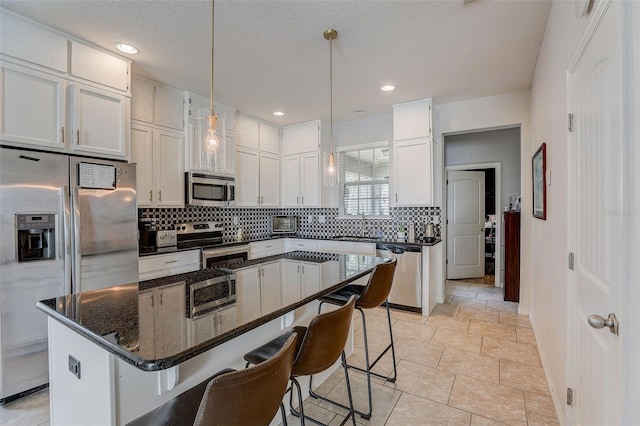 kitchen with decorative light fixtures, backsplash, appliances with stainless steel finishes, white cabinets, and a kitchen island