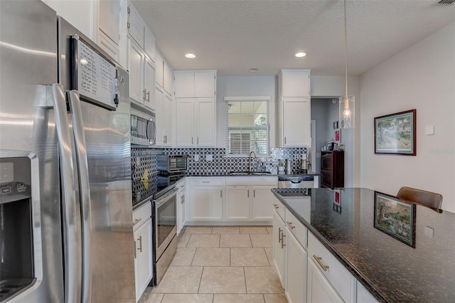 kitchen with stainless steel appliances, decorative light fixtures, dark stone counters, white cabinets, and backsplash