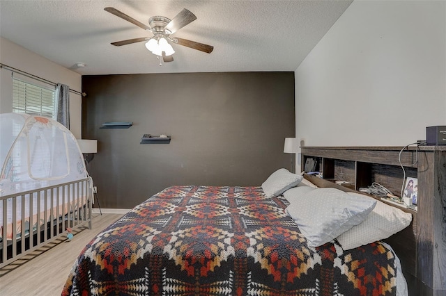 bedroom with light hardwood / wood-style floors, ceiling fan, a textured ceiling, and a fireplace