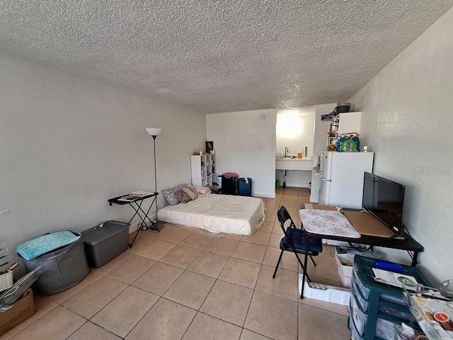 bedroom featuring white fridge, light tile floors, and a textured ceiling