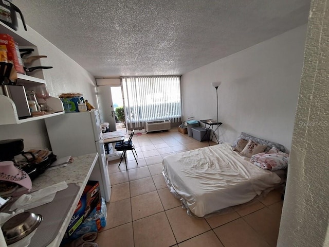 tiled bedroom featuring a wall mounted air conditioner, white fridge, and a textured ceiling