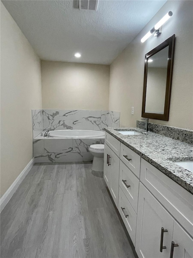 bathroom with toilet, double sink vanity, a textured ceiling, hardwood / wood-style floors, and a bath