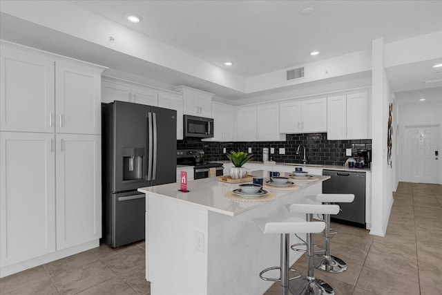 kitchen with appliances with stainless steel finishes, white cabinetry, a breakfast bar, and a kitchen island