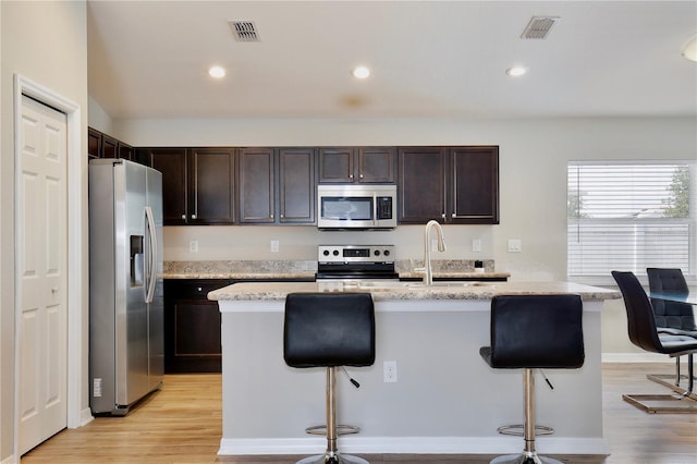 kitchen featuring dark brown cabinetry, light hardwood / wood-style flooring, appliances with stainless steel finishes, and light stone counters