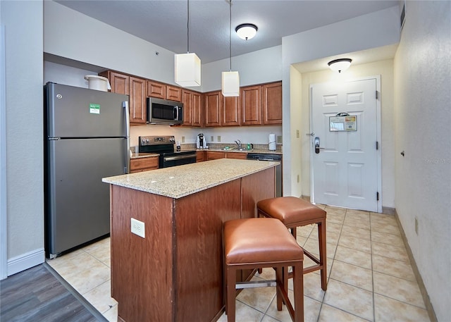 kitchen featuring a kitchen breakfast bar, a kitchen island, light stone countertops, appliances with stainless steel finishes, and hanging light fixtures