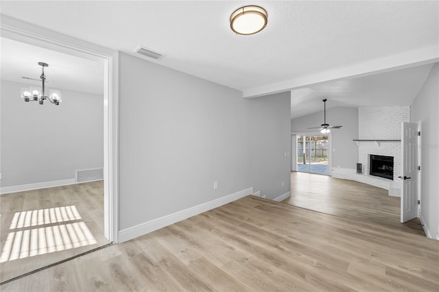 unfurnished living room with brick wall, a brick fireplace, ceiling fan with notable chandelier, lofted ceiling, and light wood-type flooring