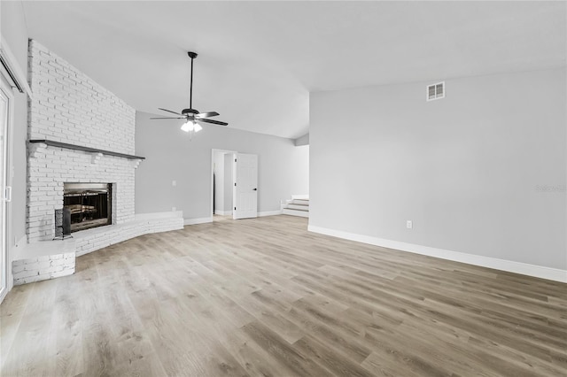 unfurnished living room with light hardwood / wood-style floors, a fireplace, brick wall, ceiling fan, and lofted ceiling