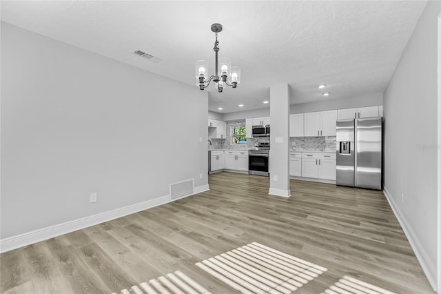 unfurnished living room with an inviting chandelier, a textured ceiling, and light wood-type flooring