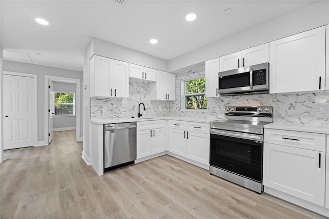 kitchen with appliances with stainless steel finishes, white cabinetry, a healthy amount of sunlight, and light hardwood / wood-style flooring