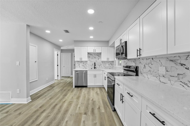 kitchen featuring light stone countertops, backsplash, appliances with stainless steel finishes, light wood-type flooring, and white cabinets