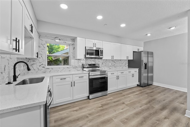 kitchen with light stone countertops, white cabinetry, appliances with stainless steel finishes, sink, and light hardwood / wood-style flooring