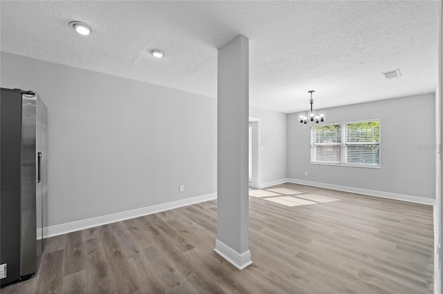 unfurnished room with a textured ceiling, wood-type flooring, and an inviting chandelier