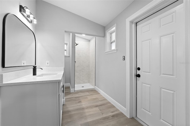 bathroom with lofted ceiling, hardwood / wood-style floors, a tile shower, and oversized vanity