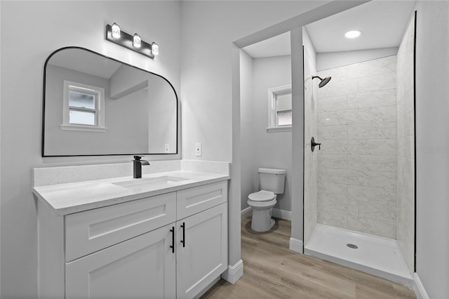 bathroom featuring a tile shower, large vanity, toilet, and wood-type flooring