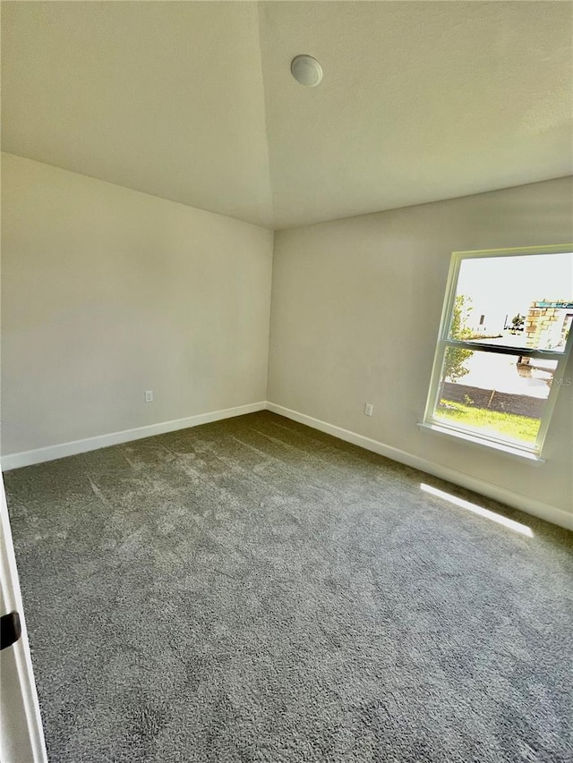 unfurnished room featuring vaulted ceiling and dark carpet