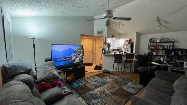 living room with a textured ceiling, ceiling fan, vaulted ceiling, and light wood-type flooring