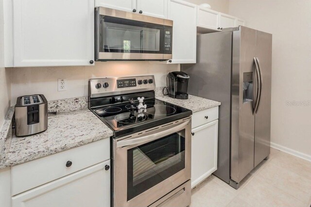 kitchen with white cabinets, appliances with stainless steel finishes, light tile floors, and light stone counters