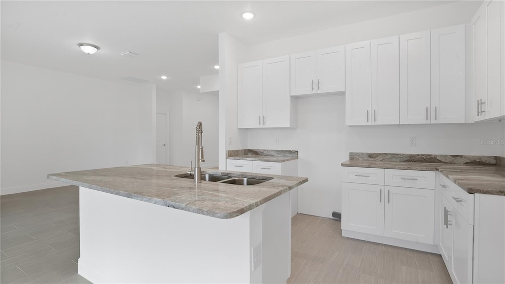 kitchen featuring light stone counters, a center island with sink, white cabinetry, and sink