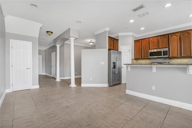 kitchen featuring light stone countertops, stainless steel appliances, tasteful backsplash, crown molding, and ornate columns