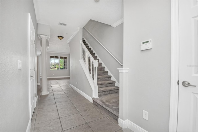 entryway with light tile flooring, ornamental molding, and decorative columns