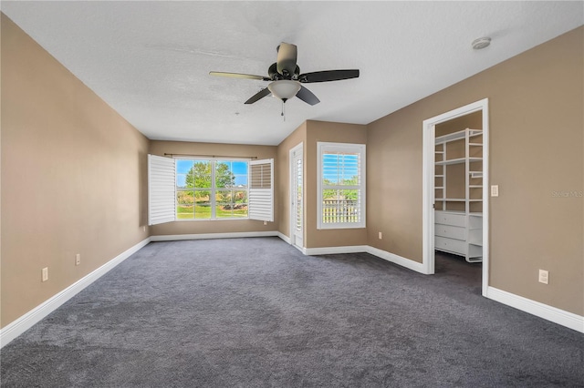 interior space featuring dark colored carpet, a walk in closet, ceiling fan, and a textured ceiling