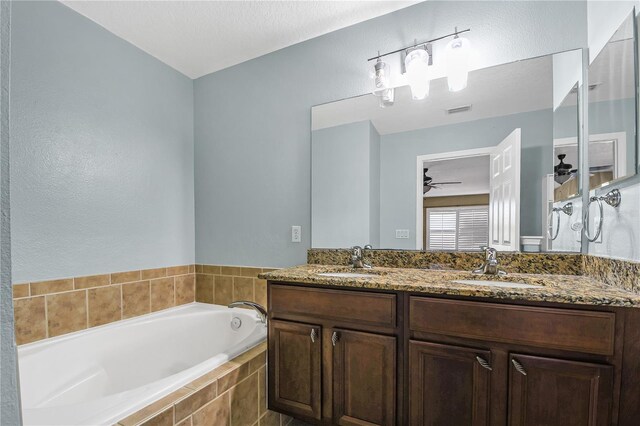 bathroom with tiled bath, double vanity, a textured ceiling, and ceiling fan