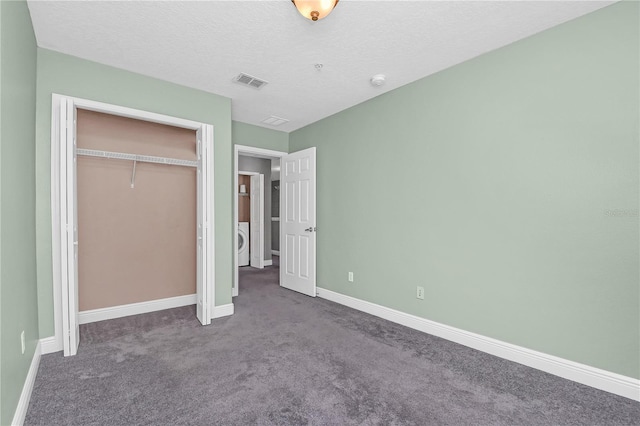 unfurnished bedroom featuring a textured ceiling, a closet, washer / dryer, and dark colored carpet