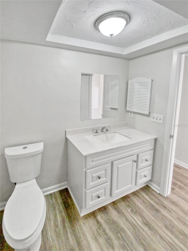 bathroom with a raised ceiling, vanity, hardwood / wood-style flooring, and toilet