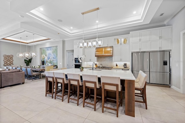 kitchen featuring a tray ceiling, a kitchen island with sink, a kitchen breakfast bar, stainless steel fridge with ice dispenser, and white cabinets