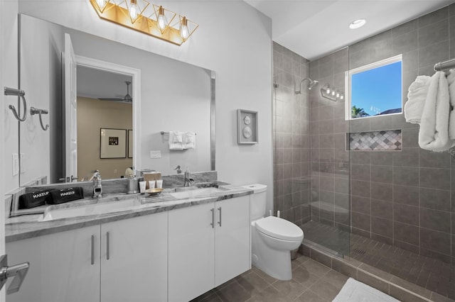 bathroom with ceiling fan, double sink vanity, a shower with door, tile flooring, and toilet