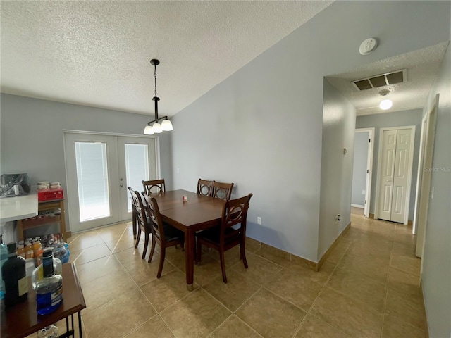 tiled dining room with french doors, a textured ceiling, a notable chandelier, and lofted ceiling