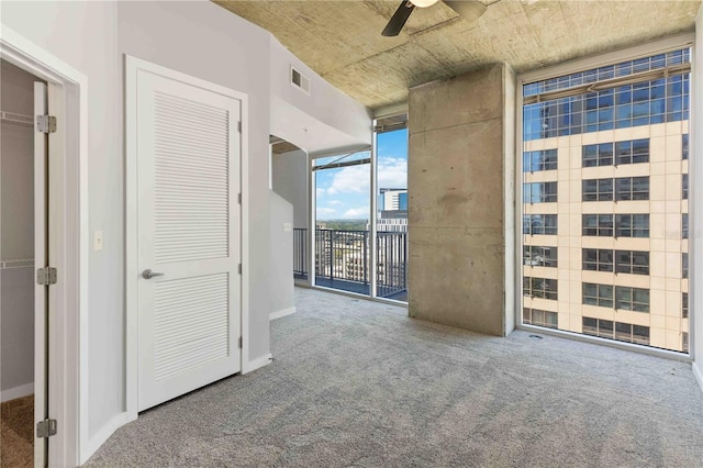 unfurnished room with a wall of windows, ceiling fan, and carpet