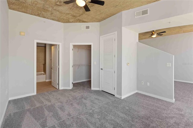 unfurnished bedroom featuring ensuite bath, a walk in closet, ceiling fan, and dark colored carpet