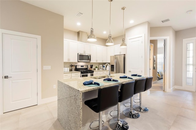 kitchen featuring an island with sink, pendant lighting, a kitchen breakfast bar, white cabinets, and appliances with stainless steel finishes