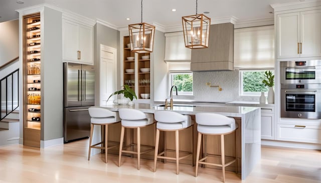 kitchen featuring light hardwood / wood-style floors, stainless steel appliances, a center island with sink, decorative light fixtures, and backsplash